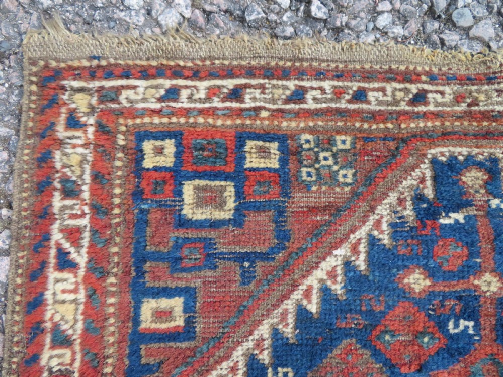 A small rectangular hand-knotted antique Khamseh rug featuring geometric tribal medallions in terracotta red, navy blue, and cream wool. View IV