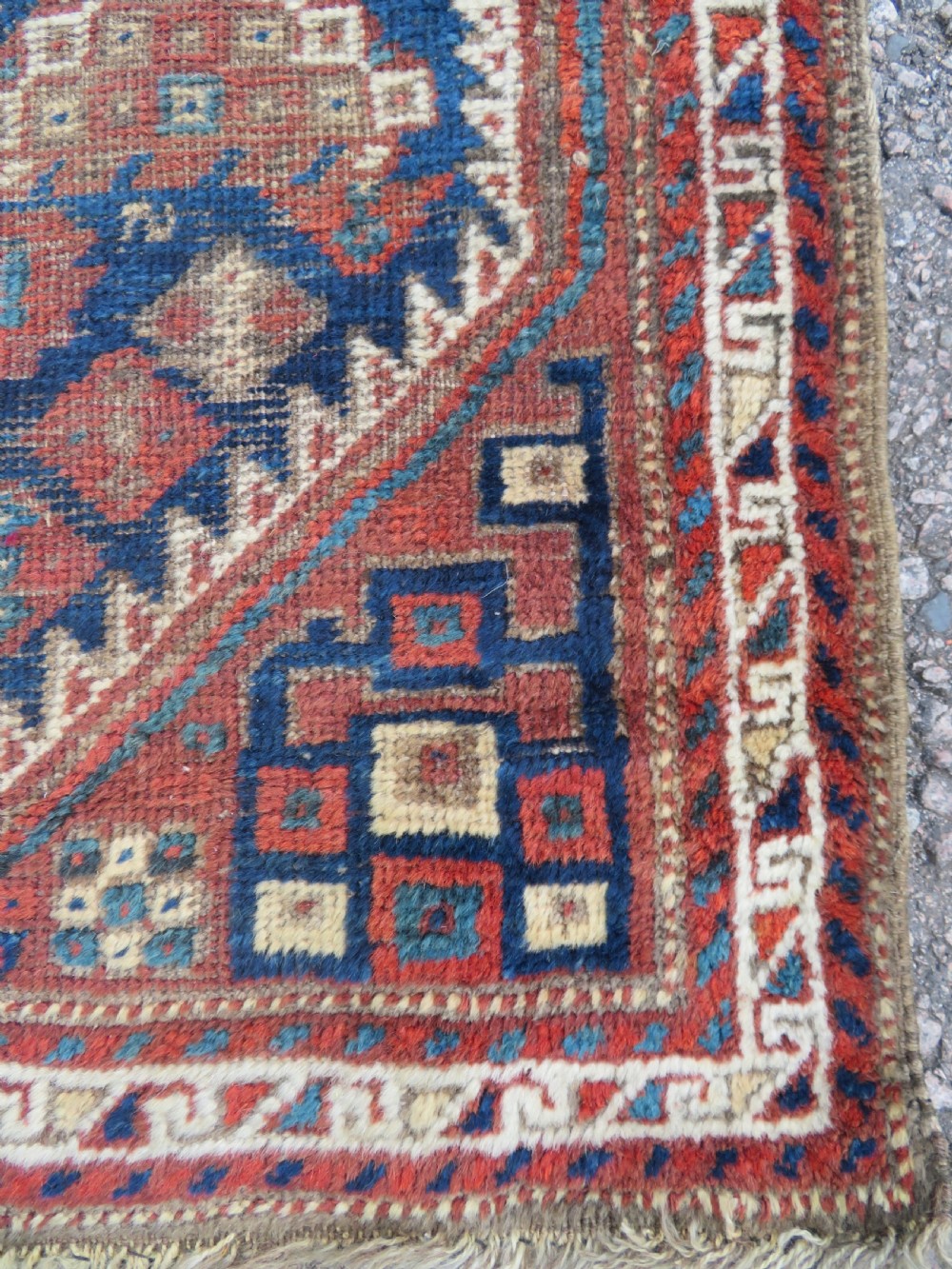 A small rectangular hand-knotted antique Khamseh rug featuring geometric tribal medallions in terracotta red, navy blue, and cream wool. View VI
