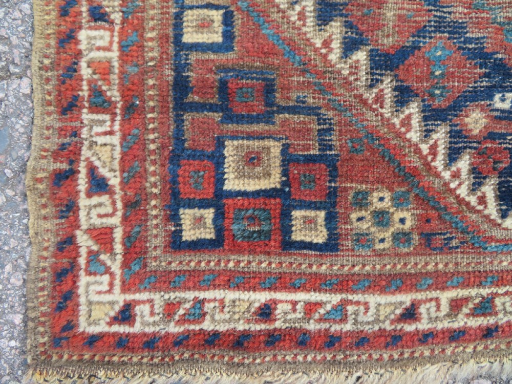 A small rectangular hand-knotted antique Khamseh rug featuring geometric tribal medallions in terracotta red, navy blue, and cream wool. View VII