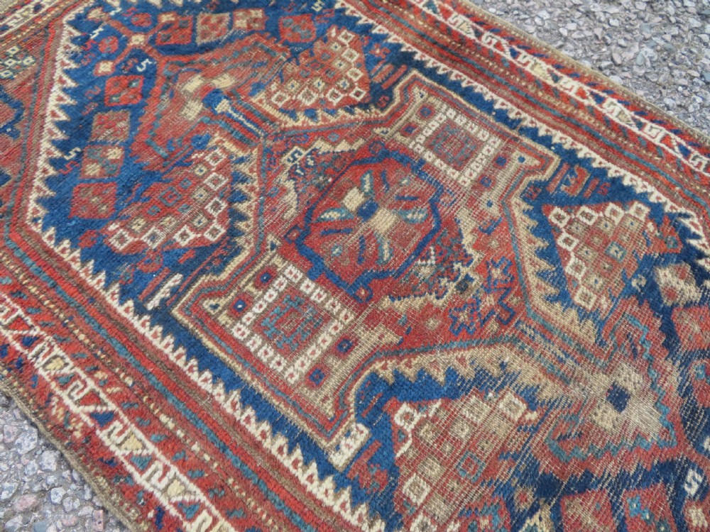 A small rectangular hand-knotted antique Khamseh rug featuring geometric tribal medallions in terracotta red, navy blue, and cream wool. View VIII