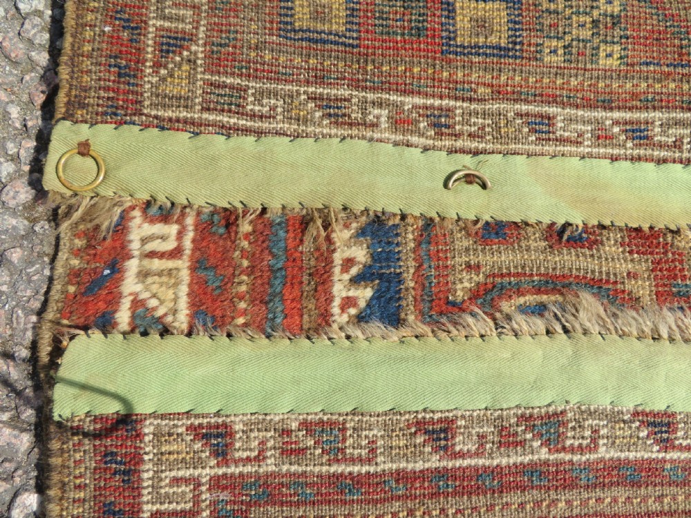 A small rectangular hand-knotted antique Khamseh rug featuring geometric tribal medallions in terracotta red, navy blue, and cream wool. View X