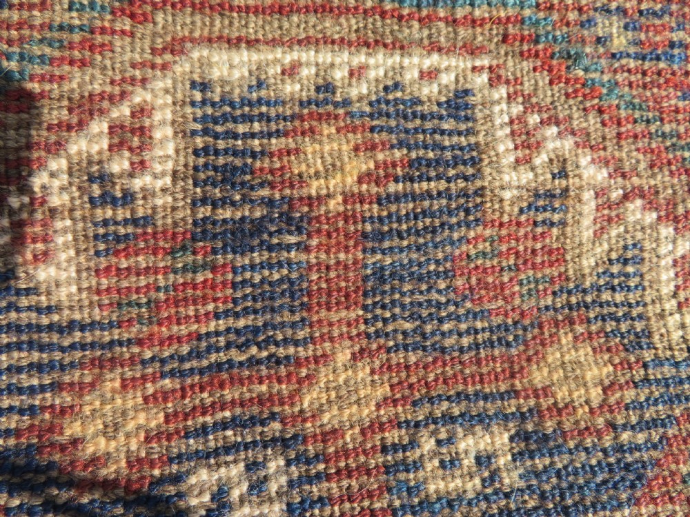 A small rectangular hand-knotted antique Khamseh rug featuring geometric tribal medallions in terracotta red, navy blue, and cream wool. View XI