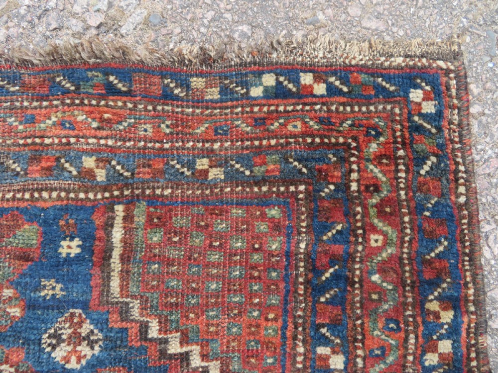 A distressed antique hand-knotted Khamseh tribal wool rug featuring three connected central medallions in red and indigo blue with geometric motifs. View II