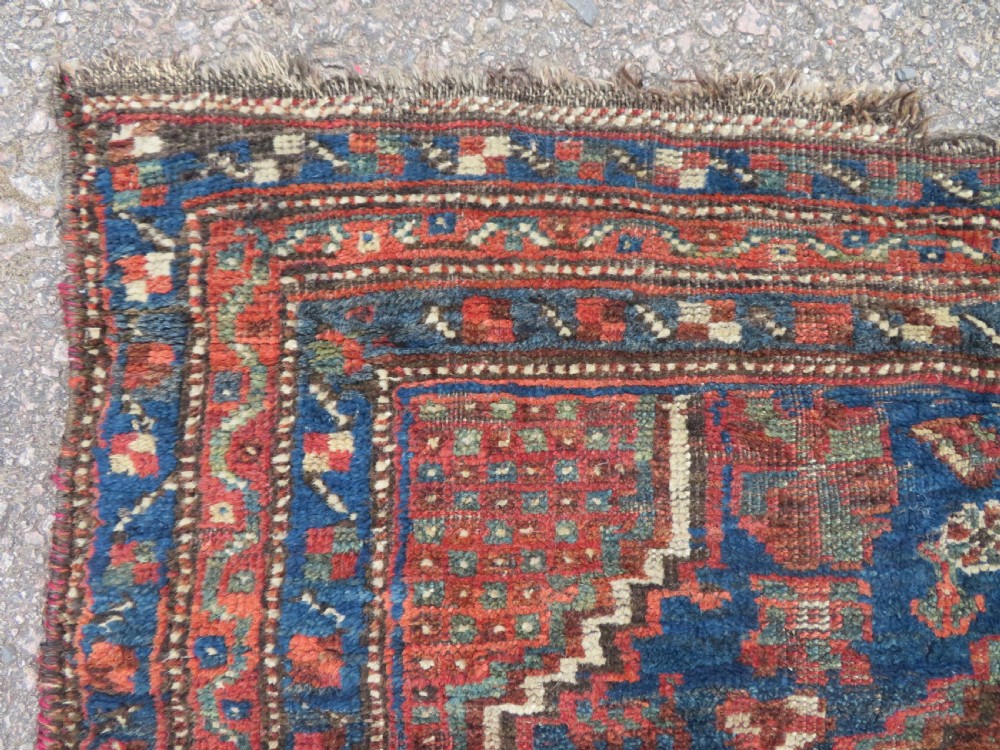 A distressed antique hand-knotted Khamseh tribal wool rug featuring three connected central medallions in red and indigo blue with geometric motifs. View IV