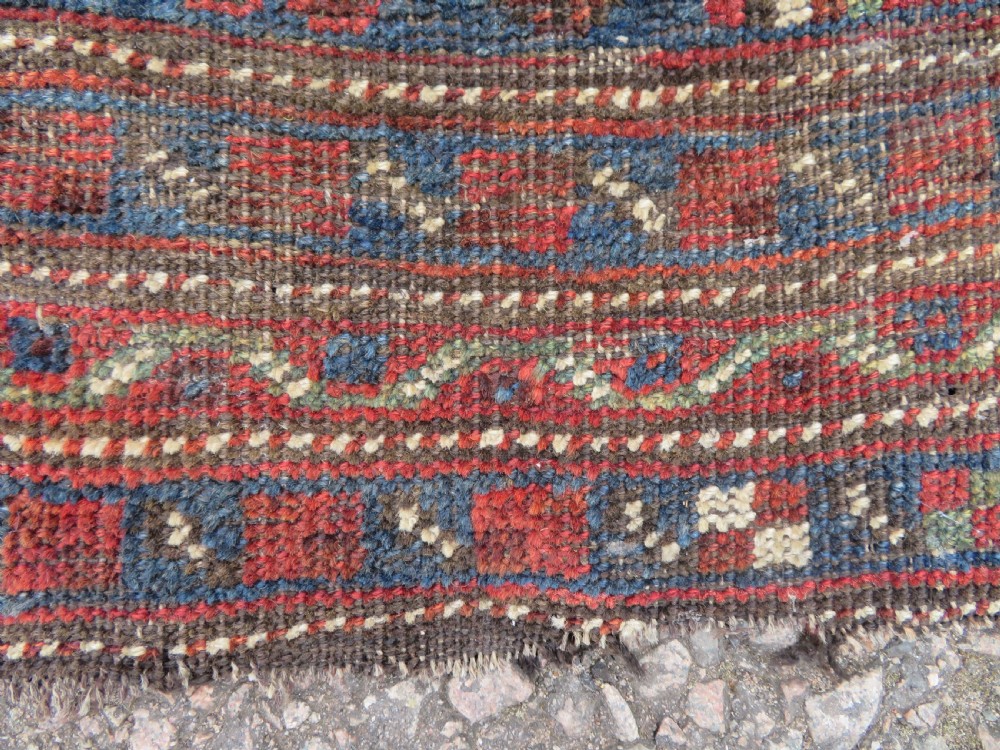 A distressed antique hand-knotted Khamseh tribal wool rug featuring three connected central medallions in red and indigo blue with geometric motifs. View VI