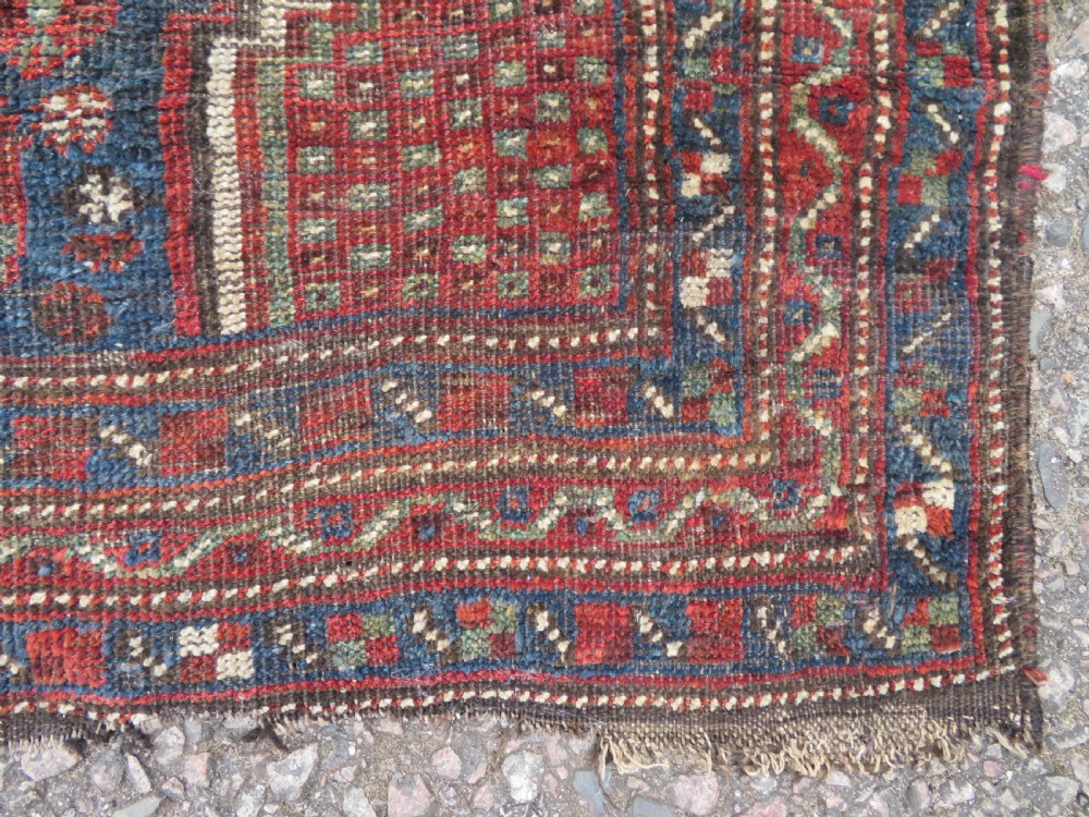 A distressed antique hand-knotted Khamseh tribal wool rug featuring three connected central medallions in red and indigo blue with geometric motifs. View VII