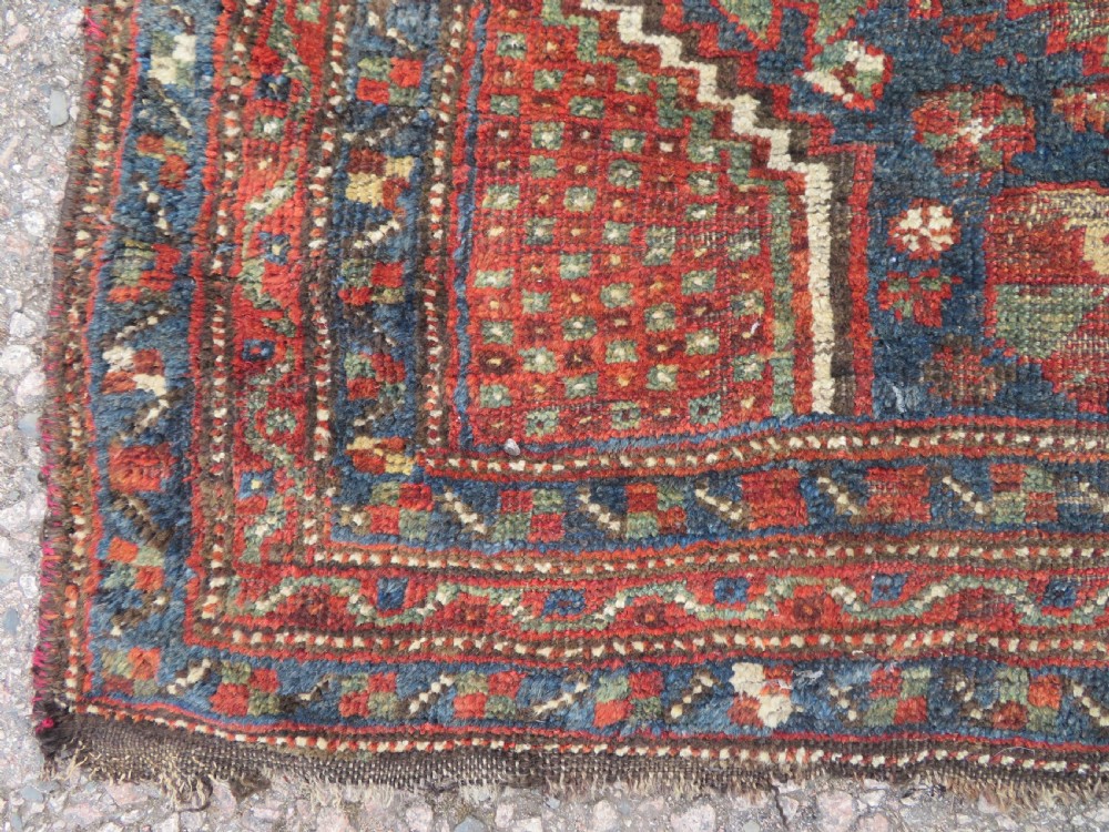 A distressed antique hand-knotted Khamseh tribal wool rug featuring three connected central medallions in red and indigo blue with geometric motifs. View VIII