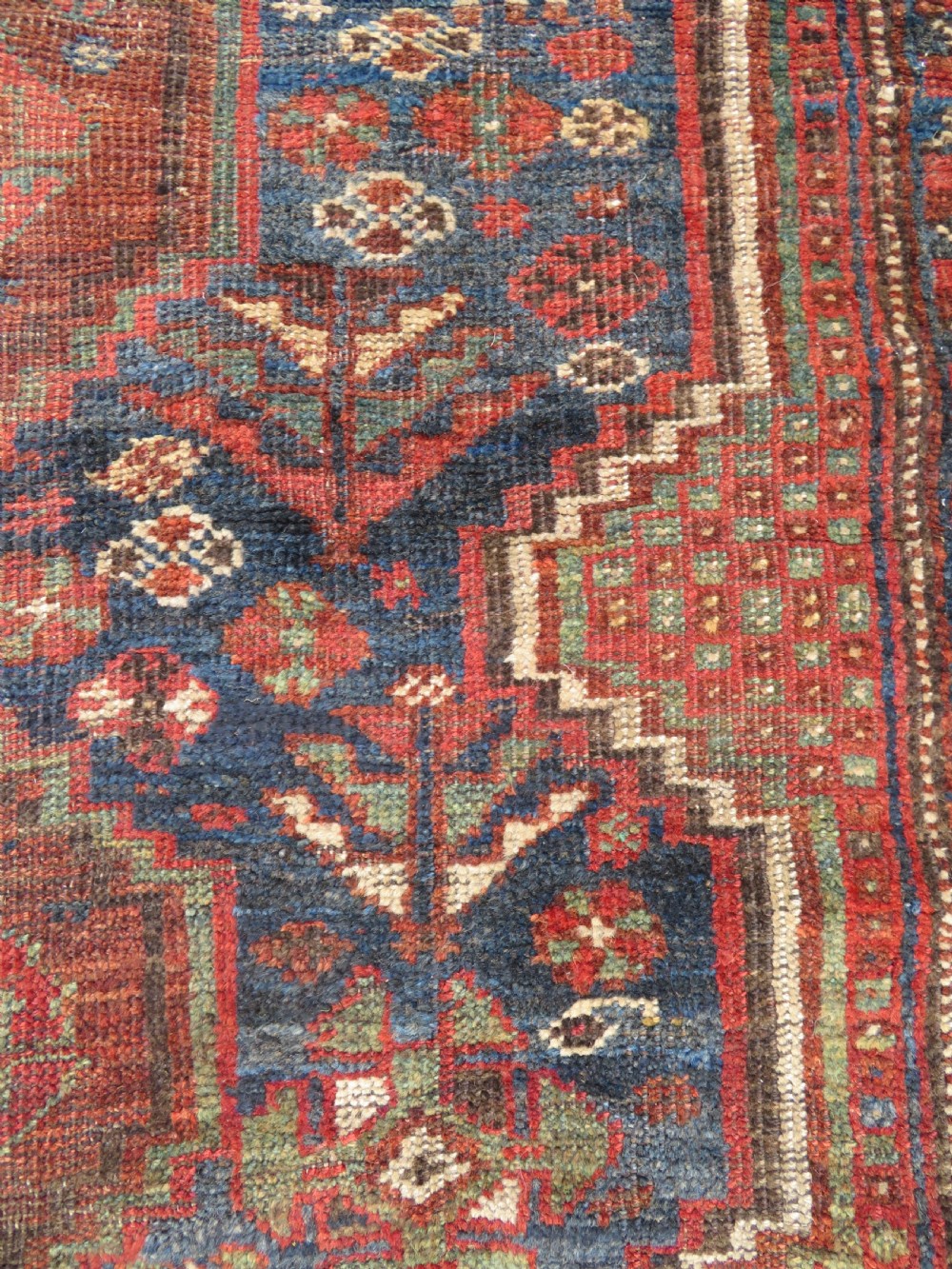 A distressed antique hand-knotted Khamseh tribal wool rug featuring three connected central medallions in red and indigo blue with geometric motifs. View IX