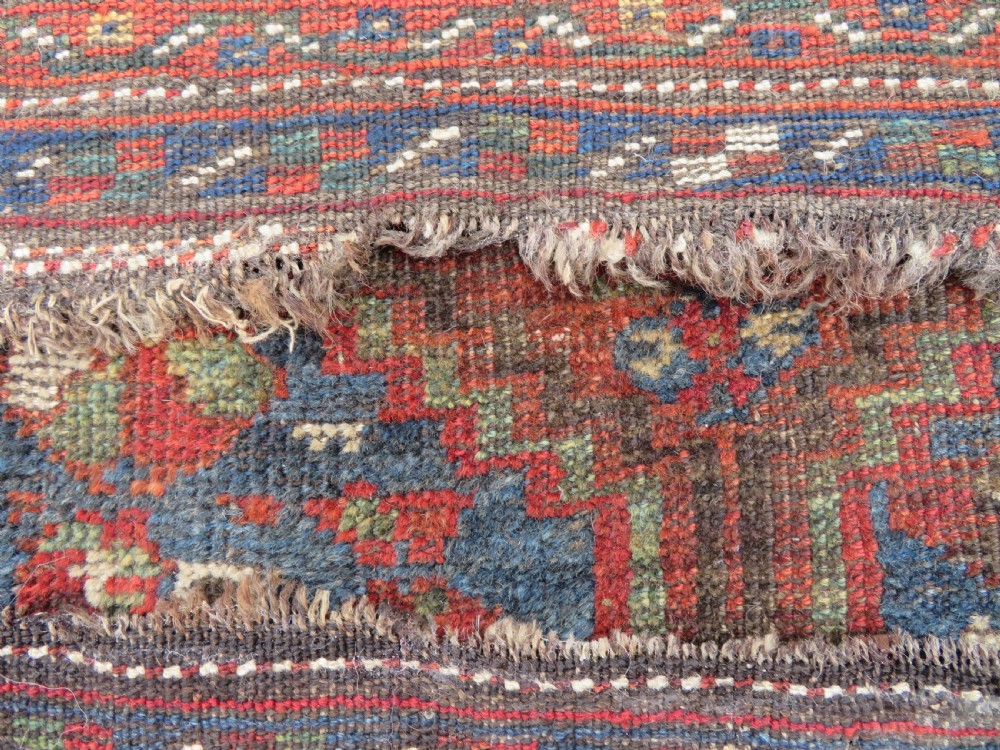 A distressed antique hand-knotted Khamseh tribal wool rug featuring three connected central medallions in red and indigo blue with geometric motifs. View XII