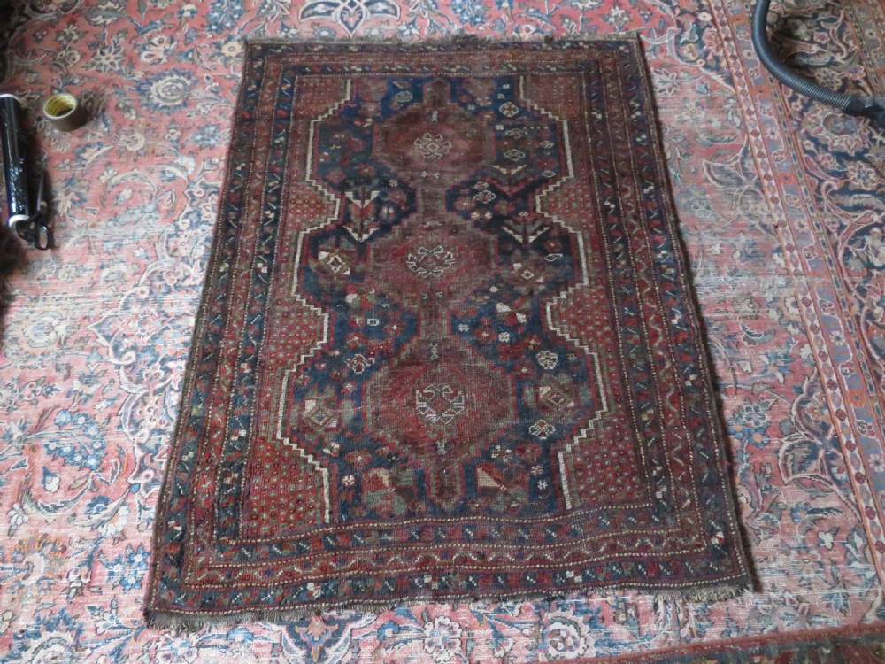 A distressed antique hand-knotted Khamseh tribal wool rug featuring three connected central medallions in red and indigo blue with geometric motifs. View XIV