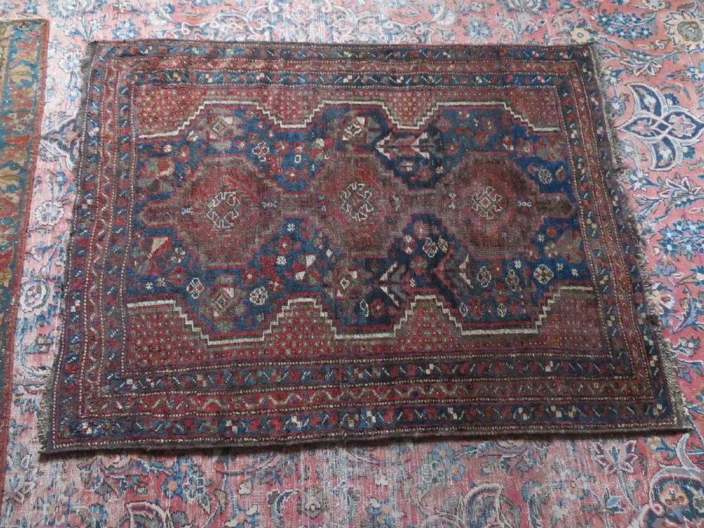 A distressed antique hand-knotted Khamseh tribal wool rug featuring three connected central medallions in red and indigo blue with geometric motifs. View XV