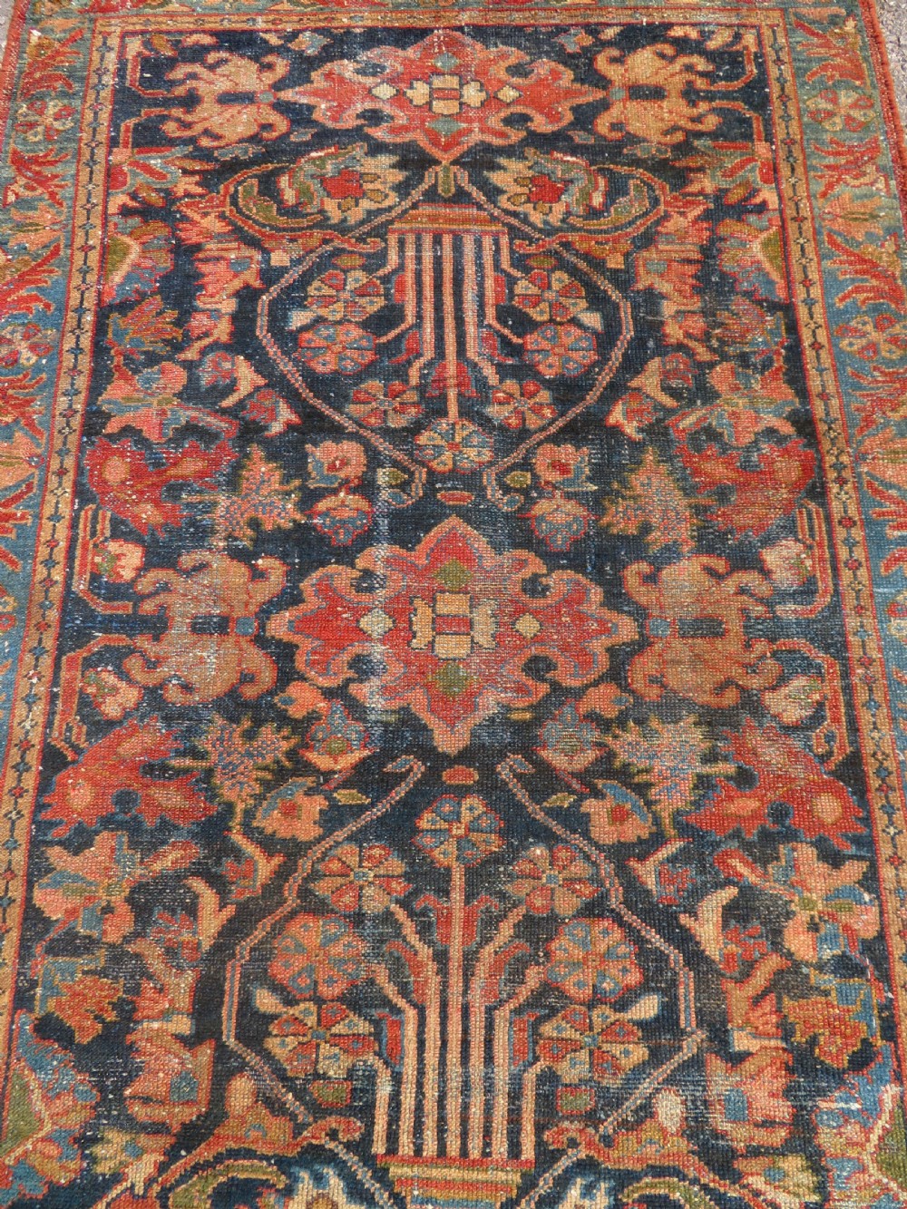A small hand-knotted antique Sarouk wool rug featuring a dark blue field with central floral medallions and a terracotta and blue border. View II