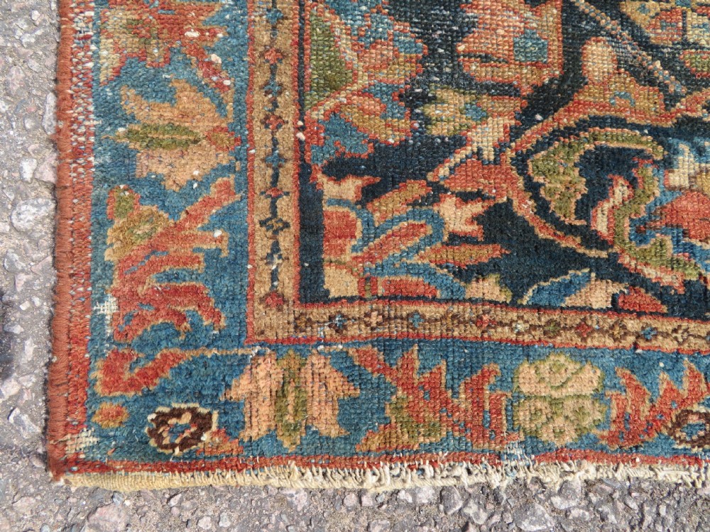 A small hand-knotted antique Sarouk wool rug featuring a dark blue field with central floral medallions and a terracotta and blue border. View III