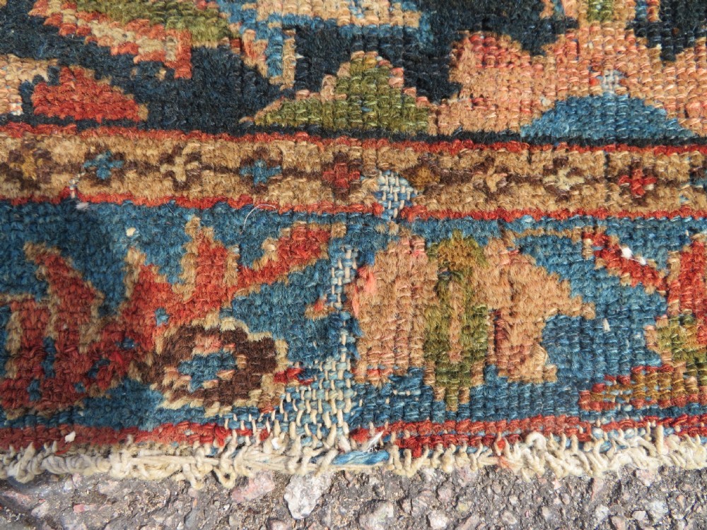 A small hand-knotted antique Sarouk wool rug featuring a dark blue field with central floral medallions and a terracotta and blue border. View IV