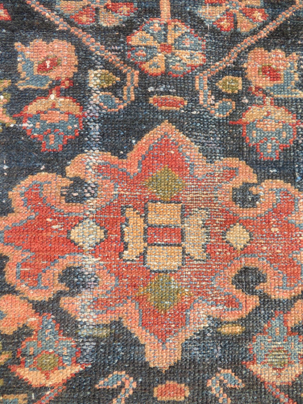 A small hand-knotted antique Sarouk wool rug featuring a dark blue field with central floral medallions and a terracotta and blue border. View VI