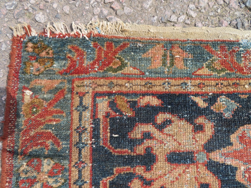 A small hand-knotted antique Sarouk wool rug featuring a dark blue field with central floral medallions and a terracotta and blue border. View VII