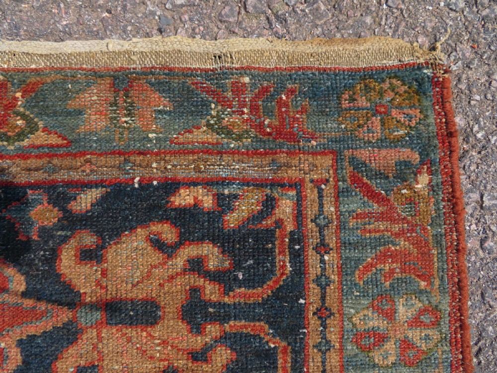 A small hand-knotted antique Sarouk wool rug featuring a dark blue field with central floral medallions and a terracotta and blue border. View VIII