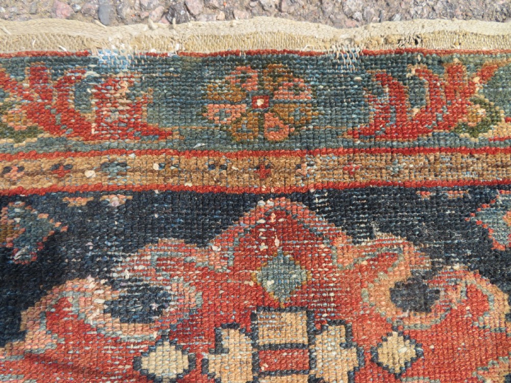 A small hand-knotted antique Sarouk wool rug featuring a dark blue field with central floral medallions and a terracotta and blue border. View IX