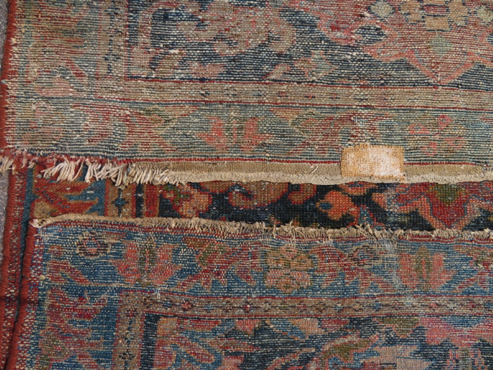 A small hand-knotted antique Sarouk wool rug featuring a dark blue field with central floral medallions and a terracotta and blue border. View XII