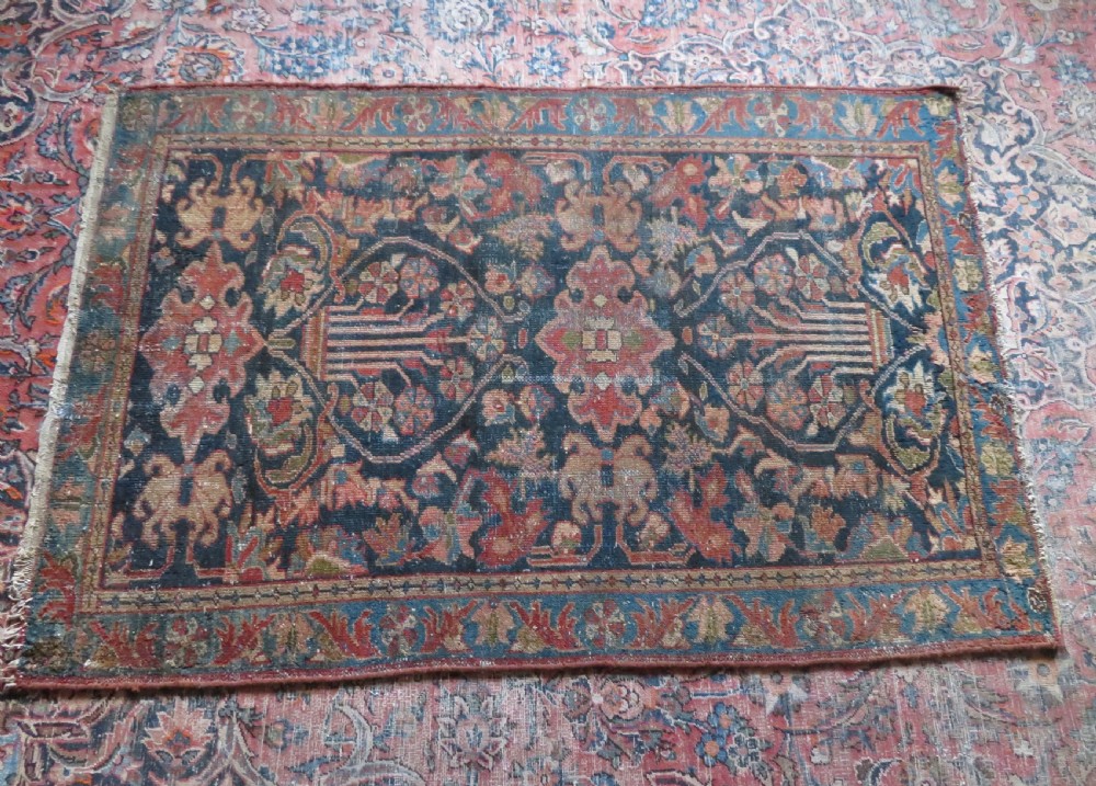 A small hand-knotted antique Sarouk wool rug featuring a dark blue field with central floral medallions and a terracotta and blue border. View XV