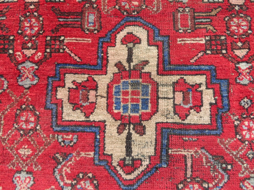 A rectangular distressed Persian Hamadan wool rug featuring a central stepped cross medallion on a crimson field with geometric borders. View III