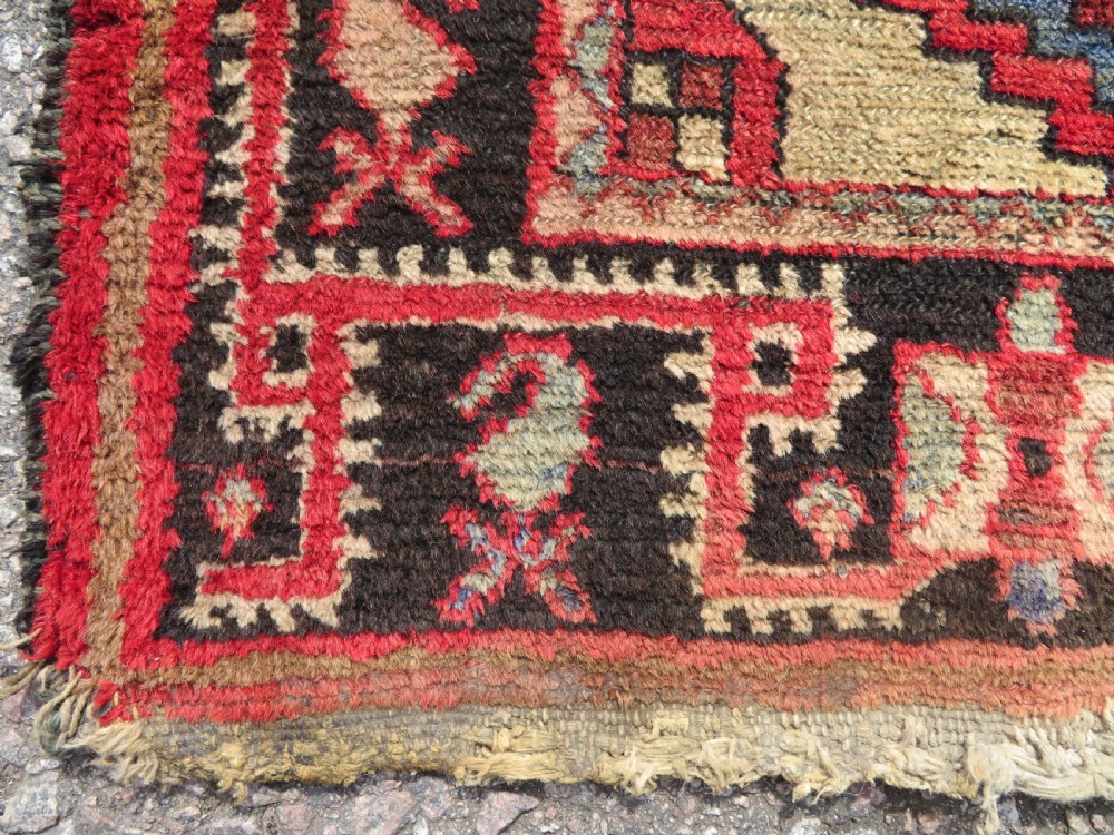 A rectangular distressed Persian Hamadan wool rug featuring a central stepped cross medallion on a crimson field with geometric borders. View IV