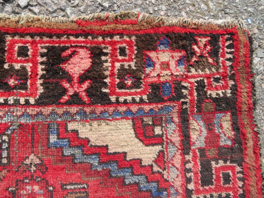 A rectangular distressed Persian Hamadan wool rug featuring a central stepped cross medallion on a crimson field with geometric borders. View X