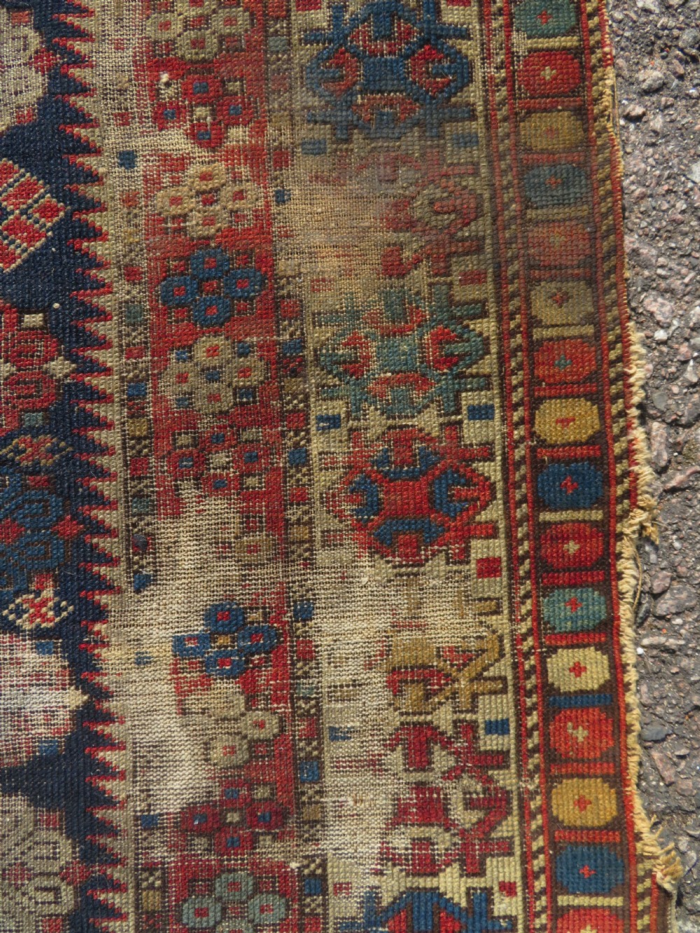 A rectangular hand-knotted antique Caucasian Daghestan rug featuring geometric medallions, intricate borders, and a distressed surface in red and navy blue tones. View IX