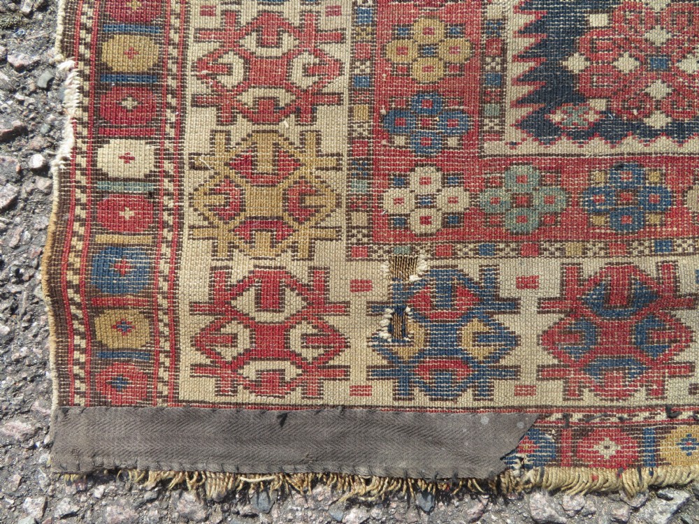 A rectangular hand-knotted antique Caucasian Daghestan rug featuring geometric medallions, intricate borders, and a distressed surface in red and navy blue tones. View XIII