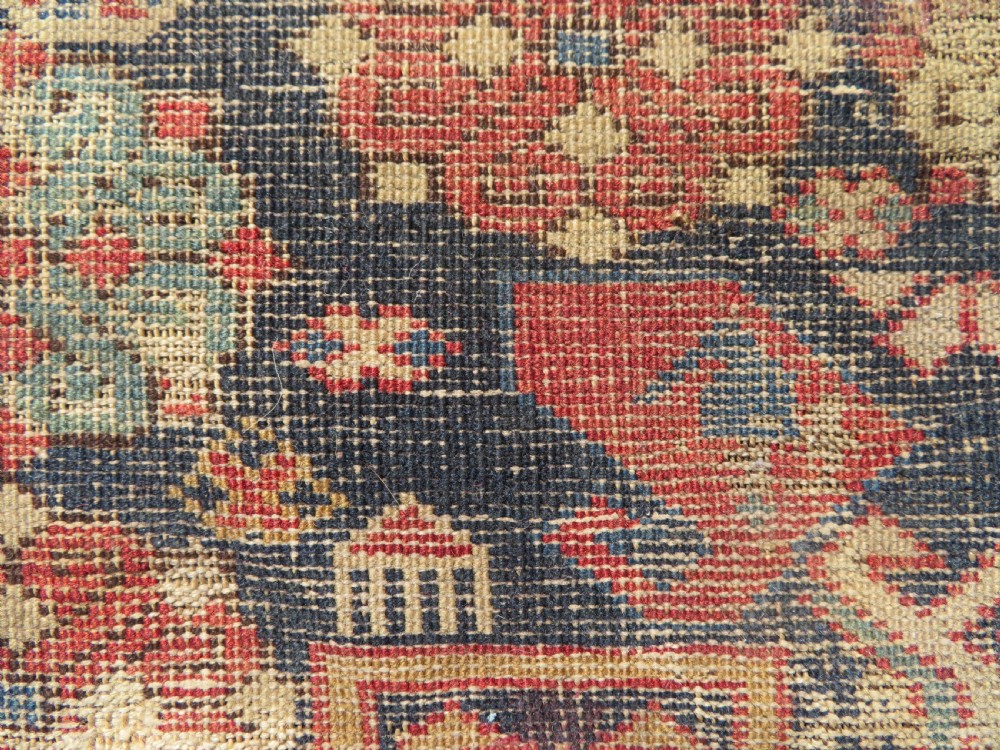 A rectangular hand-knotted antique Caucasian Daghestan rug featuring geometric medallions, intricate borders, and a distressed surface in red and navy blue tones. View XVI
