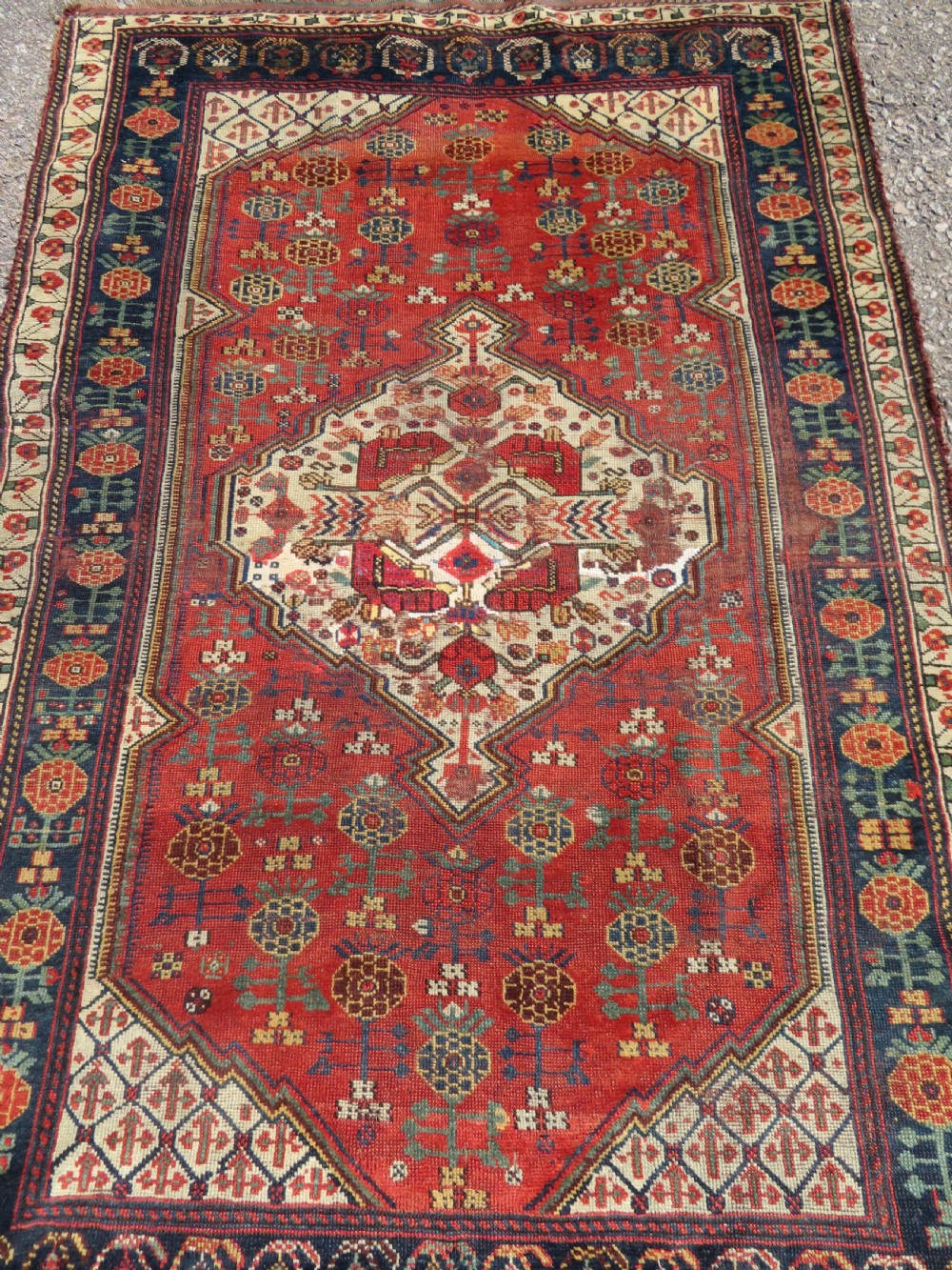 An antique hand-knotted Khamseh wool rug featuring a red central field with a geometric medallion framed by navy blue and cream borders. View II