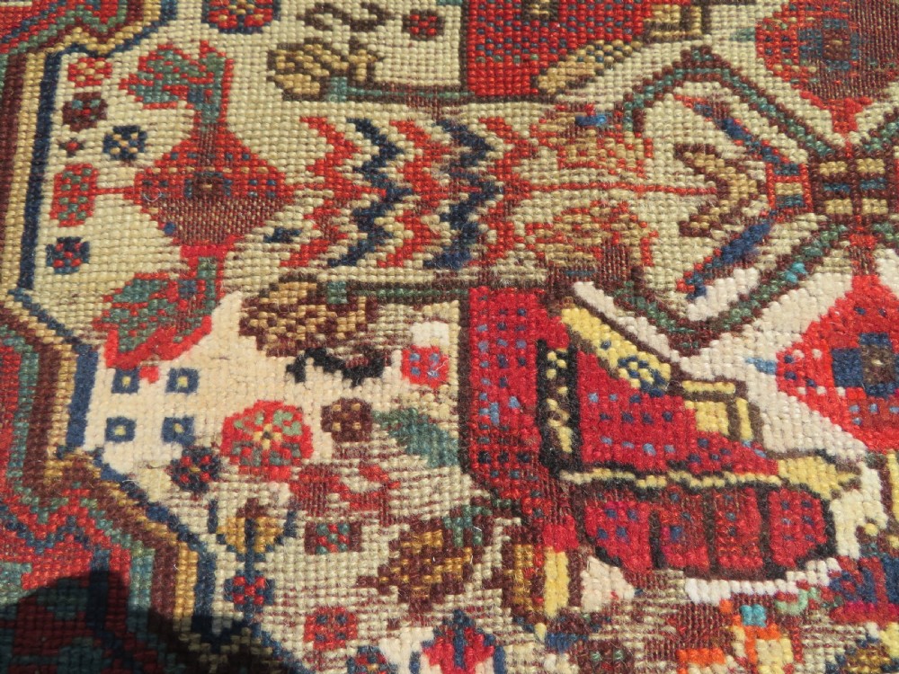 An antique hand-knotted Khamseh wool rug featuring a red central field with a geometric medallion framed by navy blue and cream borders. View V
