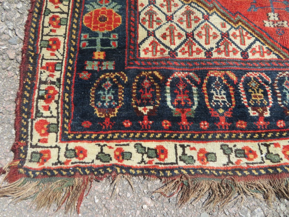 An antique hand-knotted Khamseh wool rug featuring a red central field with a geometric medallion framed by navy blue and cream borders. View VI