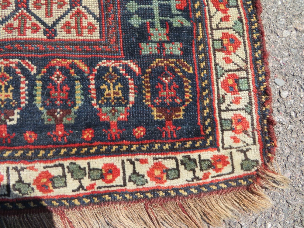 An antique hand-knotted Khamseh wool rug featuring a red central field with a geometric medallion framed by navy blue and cream borders. View VII