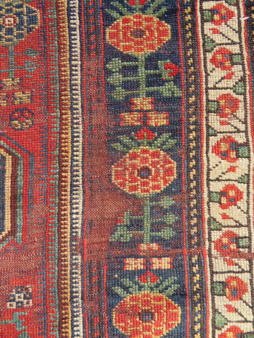 An antique hand-knotted Khamseh wool rug featuring a red central field with a geometric medallion framed by navy blue and cream borders. View VIII