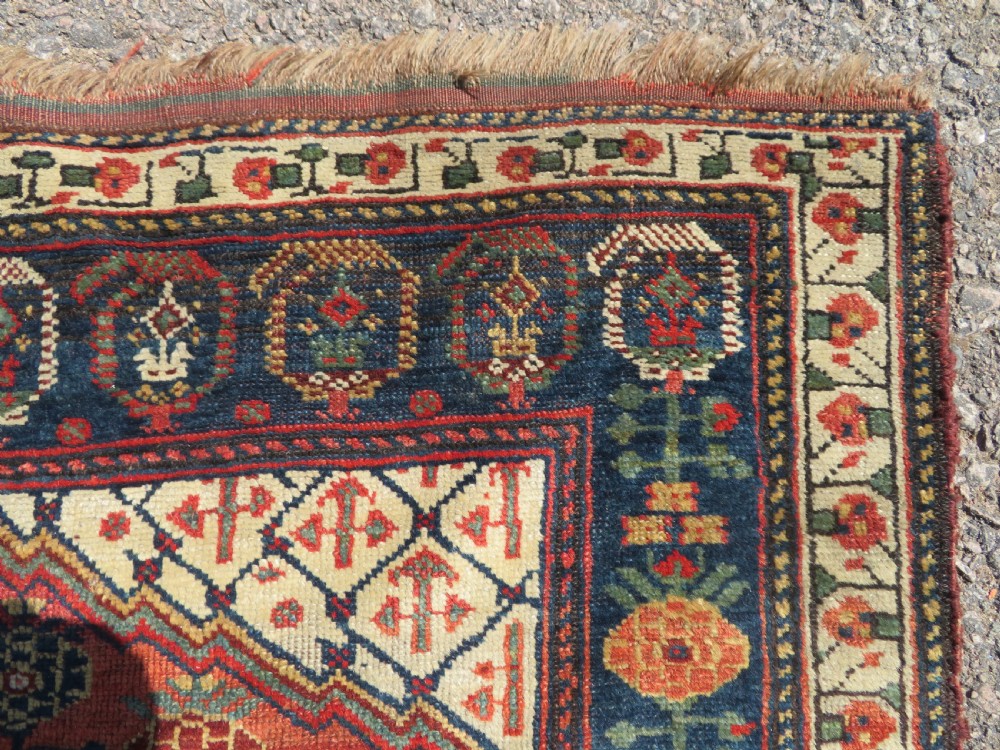 An antique hand-knotted Khamseh wool rug featuring a red central field with a geometric medallion framed by navy blue and cream borders. View IX