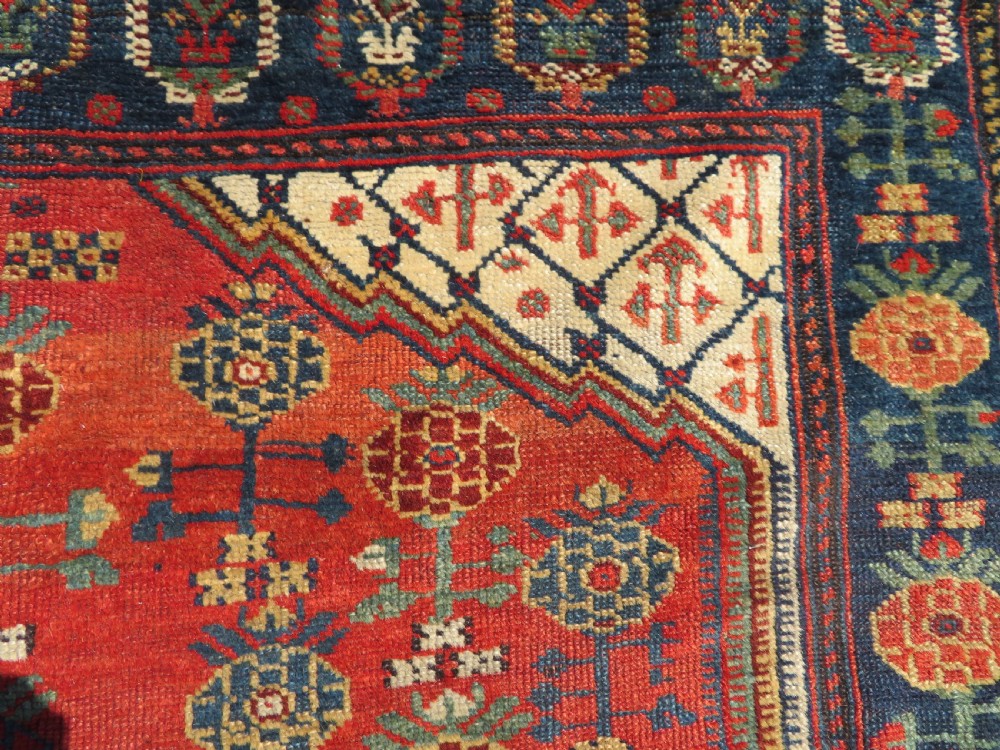 An antique hand-knotted Khamseh wool rug featuring a red central field with a geometric medallion framed by navy blue and cream borders. View XI