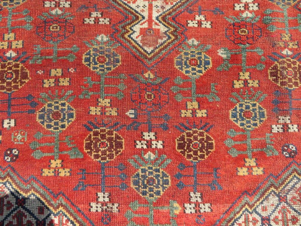 An antique hand-knotted Khamseh wool rug featuring a red central field with a geometric medallion framed by navy blue and cream borders. View XIII