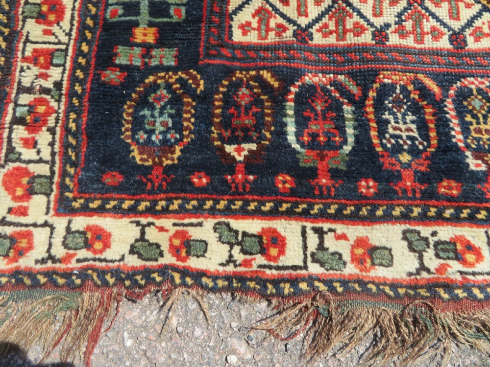 An antique hand-knotted Khamseh wool rug featuring a red central field with a geometric medallion framed by navy blue and cream borders. View XIV