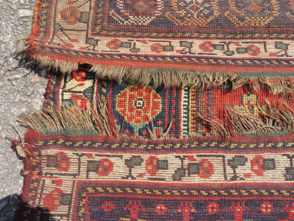 An antique hand-knotted Khamseh wool rug featuring a red central field with a geometric medallion framed by navy blue and cream borders. View XVI