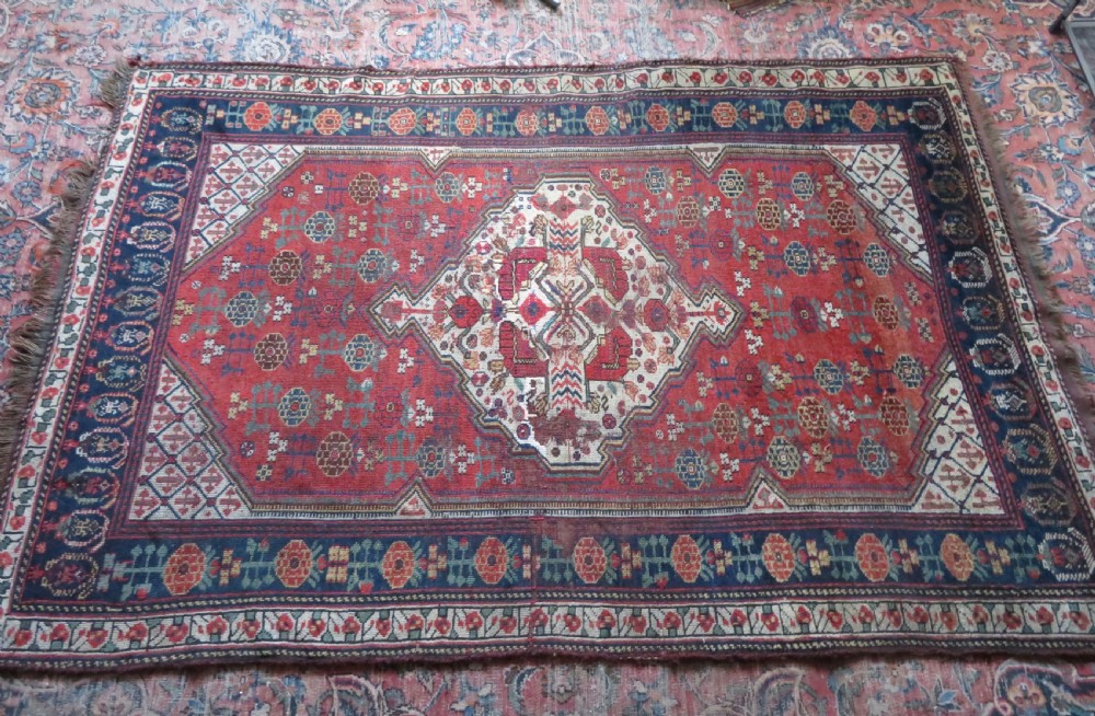 An antique hand-knotted Khamseh wool rug featuring a red central field with a geometric medallion framed by navy blue and cream borders. View XXI