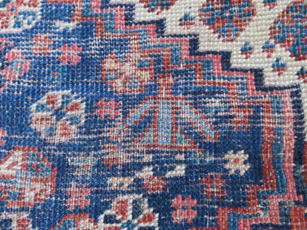 Distressed hand-knotted South Persian Khamseh tribal rug featuring nested diamond medallions, stylized animal motifs, and a multi-banded geometric border in navy blue, terracotta, and cream. View VI