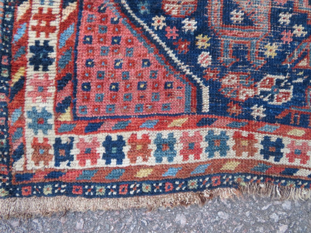 Distressed hand-knotted South Persian Khamseh tribal rug featuring nested diamond medallions, stylized animal motifs, and a multi-banded geometric border in navy blue, terracotta, and cream. View VIII