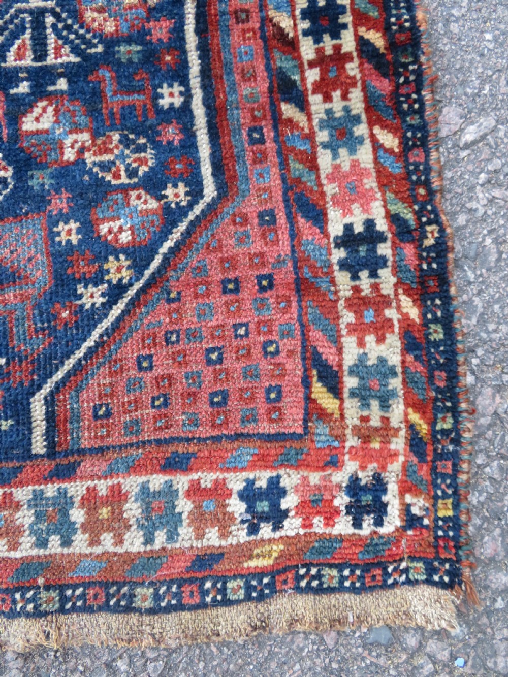 Distressed hand-knotted South Persian Khamseh tribal rug featuring nested diamond medallions, stylized animal motifs, and a multi-banded geometric border in navy blue, terracotta, and cream. View X