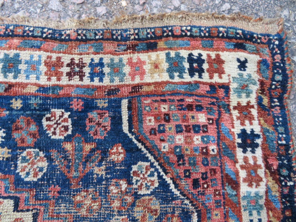 Distressed hand-knotted South Persian Khamseh tribal rug featuring nested diamond medallions, stylized animal motifs, and a multi-banded geometric border in navy blue, terracotta, and cream. View XI