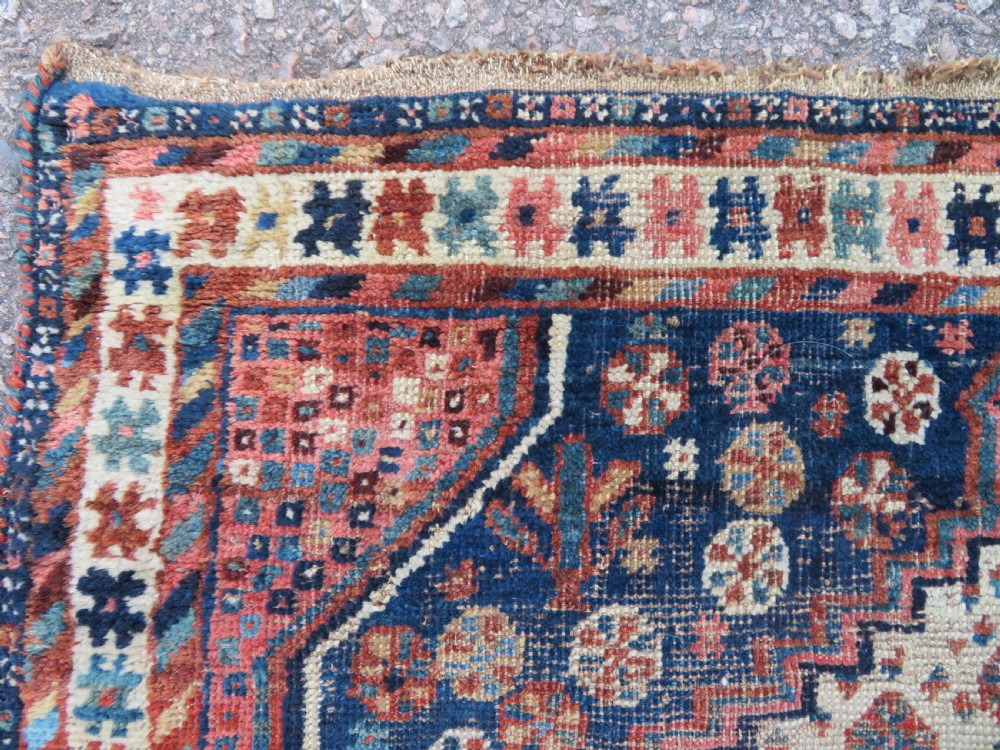 Distressed hand-knotted South Persian Khamseh tribal rug featuring nested diamond medallions, stylized animal motifs, and a multi-banded geometric border in navy blue, terracotta, and cream. View XII