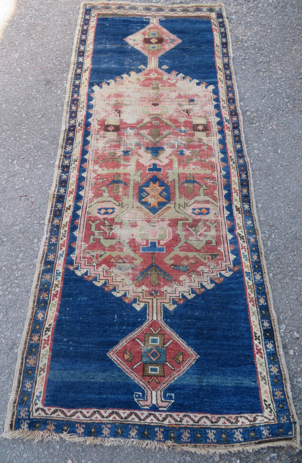 An antique hand-woven Turkish runner rug featuring indigo blue ends and a distressed red and cream geometric central medallion pattern.