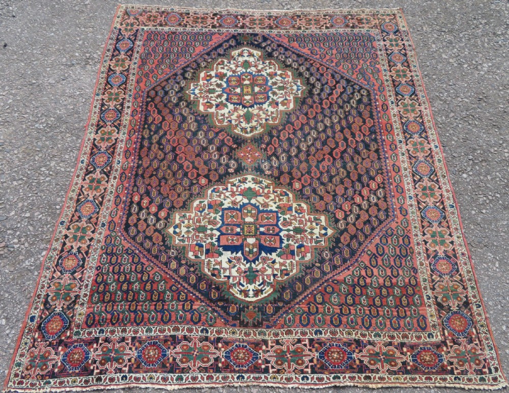 A hand-knotted Bakhtiari tribal wool rug with central ivory and blue medallions framed by a dark navy field with repeating boteh patterns and a detailed geometric border.