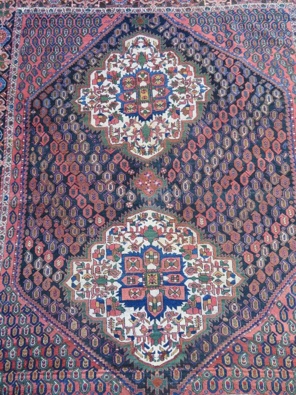 A hand-knotted Bakhtiari tribal wool rug with central ivory and blue medallions framed by a dark navy field with repeating boteh patterns and a detailed geometric border. View II