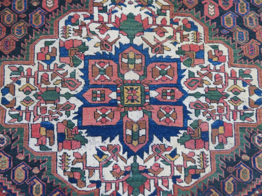 A hand-knotted Bakhtiari tribal wool rug with central ivory and blue medallions framed by a dark navy field with repeating boteh patterns and a detailed geometric border. View IV